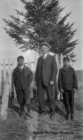 Two boys and man standing near the old mission at Onion Lake, Saskatchewan